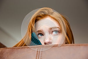 Unconfident shy redhead girl peeping from sofa photo