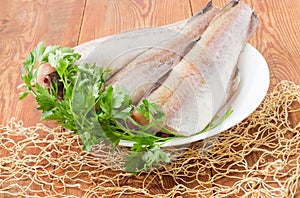 Uncooked Alaska pollock carcasses with parsley on dish