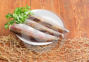 Uncooked Alaska pollock carcasses on wooden surface with fishing