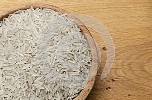 Uncooked basmati rice in a wooden bowl on a wooden table.