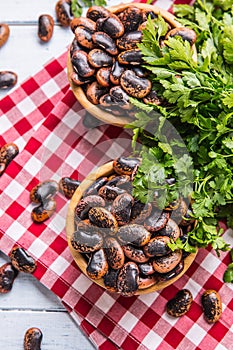 Uncooked beans in wooden bowles with parsley herbs on kitchen table