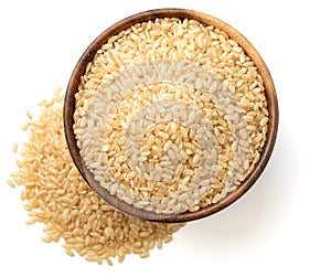 Uncooked brown rice in the wooen bowl, isolated on the white background, top view