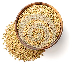 Uncooked buckwheat in the wooden bowl, isolated on the white background, top view