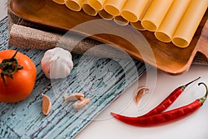 Uncooked cannelloni pasta on cutting board and ingredients. Italian cuisine