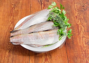 Uncooked carcasses of the Alaska pollock and parsley on dish