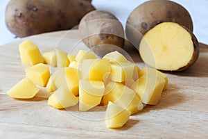 Uncooked cubical yellow potatoes and fresh raw potatoes on chopping board.