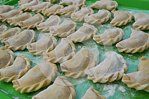 Uncooked dumplings on a green kitchen tray with flour