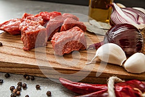 Uncooked fresh diced beef meat with herbs and oil on an old rustic wooden kitchen board over stone background.