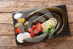 Uncooked fresh eel with spices, vegetables and lemon close up on a slate board. horizontal top view