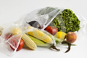 Uncooked,fresh vegetables and fruits in plastic shopping bags on white background with copy space.