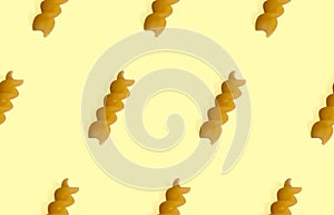 Uncooked fusilli pasta isolated on yellow seamless pattern. Itallian spiral pasta close-up on orange seamless background