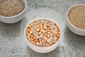 Uncooked half peas, millet and rice in white ceramic bowls on metal background