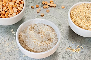 Uncooked half peas, rice and millet in white ceramic bowl above view on metal background