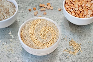 Uncooked half peas, rice and millet in white ceramic bowls on metal background