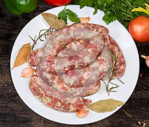 Uncooked homemade pork sausages and spices on dish, top view