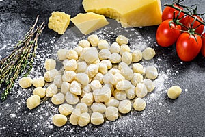 Uncooked homemade potato gnocchi with ingredients for cooking pasta. Black background. Top view