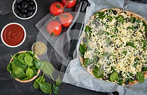 Uncooked homemade vegan pizza with spinach, tomatoes, black oliv