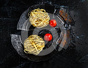 Uncooked Italian Fettuccine Pasta on a Broken Black Plate with Cherry Tomatoes