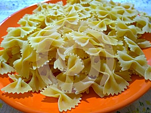 Uncooked italian pasta farfalle on an orange plate. Bow-tie pasta or butterfly macaroni. Strichetti or farfalloni. Home cooking. F