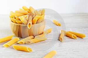 Uncooked italian pasta penne on wooden cup and wood background