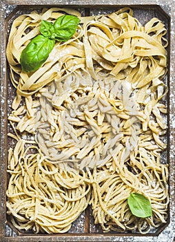 Uncooked Italian pasta in wooden tray with basil and flour