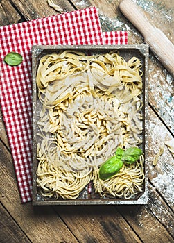 Uncooked Italian pasta in wooden tray over rustic background