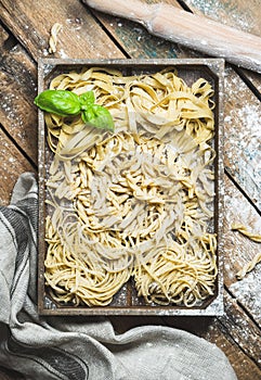 Uncooked Italian pasta in wooden tray over shabby background