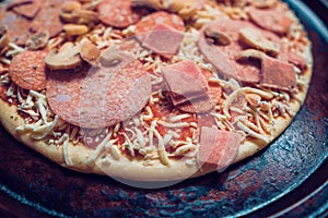 Uncooked meat feast pizza on a metal round tray on traditional red tile surface. Italian style food. Cook from frozen product.