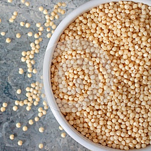 Uncooked millet seeds in white ceramic bowl on metal background