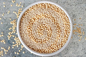 Uncooked millet in white ceramic bowl on metal background view from above