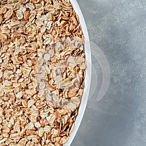 Uncooked oat flakes in a white bowl on a gray background. Close up, top view of natural organic product.