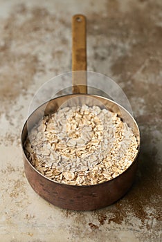 Uncooked Oatmeal in Copper Saucepan on Grunge Stainless Steel Surface