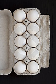 Uncooked Organic White Eggs in a paper box on a black surface, top view. Flat lay, overhead, from above