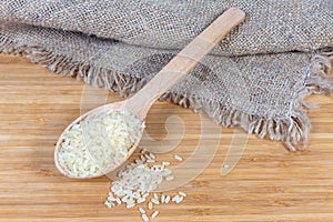 Uncooked parboiled rice in the wooden spoon on wooden surface