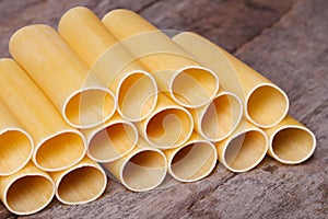 Uncooked pasta cannelloni on an old wooden board.