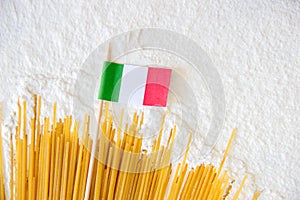 Uncooked pasta spaghetti macaroni and small italian flag on white floured background