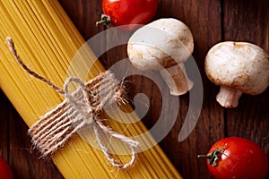 Uncooked pasta, tomatoes and mushrooms on wooden background, top view, close-up, selective focus