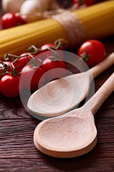 Uncooked pasta, tomatoes and two spoons on wooden background, top view, close-up, shallow depth of field