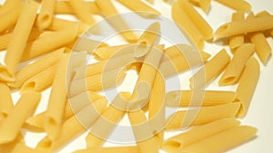 Uncooked penne pasta falling on white surface slow motion,kitchen food background