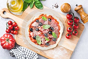 Uncooked Pizza with tomato sauce, prosciutto and olives