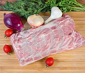 Uncooked pork loin among vegetables on cutting board, top view