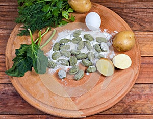 Uncooked potato gnocchi with spinach, ingredients on round wooden board photo