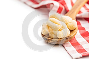 Uncooked potato gnocchi in wooden spoon isolated on white background