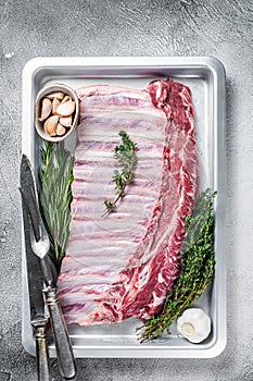 Uncooked raw rack of lamb ribs in baking dish with herbs. White background. Top view