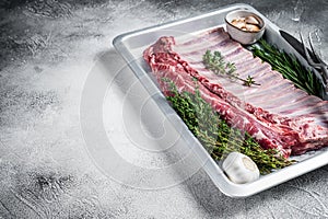 Uncooked raw rack of lamb ribs in baking dish with herbs. White background. Top view. Copy space