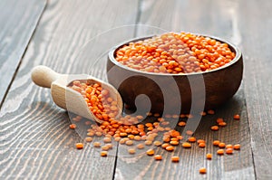 Uncooked raw red lentil in wooden shovel or bowl on wooden background