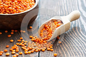 Uncooked raw red lentil in wooden shovel or bowl on wooden background