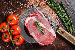 Uncooked raw Rib eye Steak, ribeye beef meat on butcher cleaver with herbs. Dark background. Top view