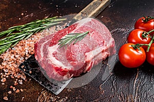 Uncooked raw Rib eye Steak, ribeye beef meat on butcher cleaver with herbs. Dark background. Top view