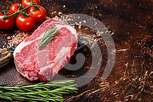 Uncooked raw Rib eye Steak, ribeye beef meat on butcher cleaver with herbs. Dark background. Top view. Copy space